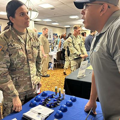 A man in a ball cap talks to a soldier in uniform